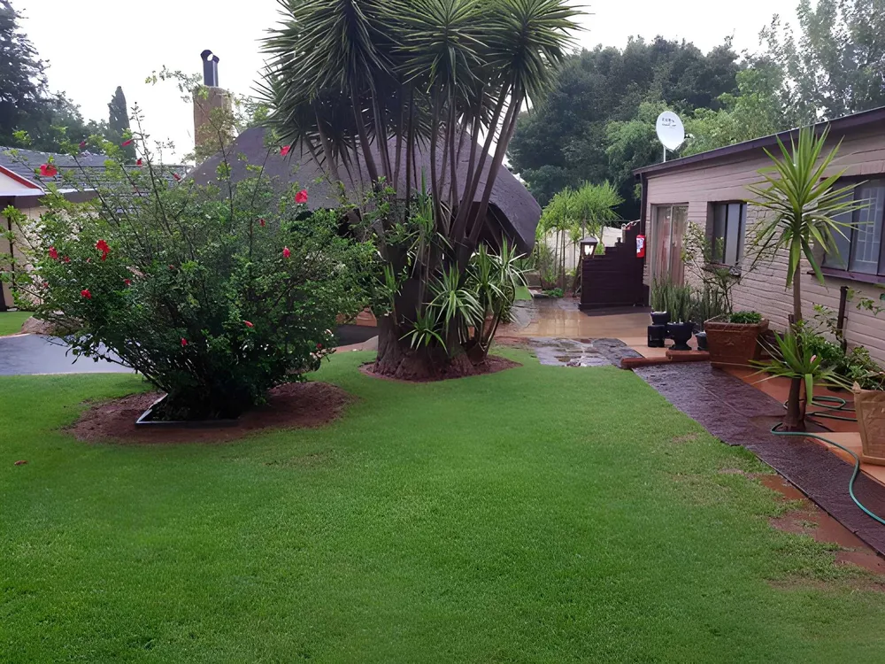 Green lawn, flowering shrubs and the thatched lapa at Eden Vreugd